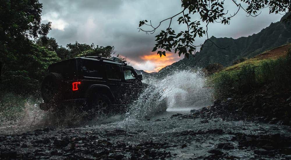A black 2018 Jeep Wrangler Unlimited is driving through a river in the woods.
