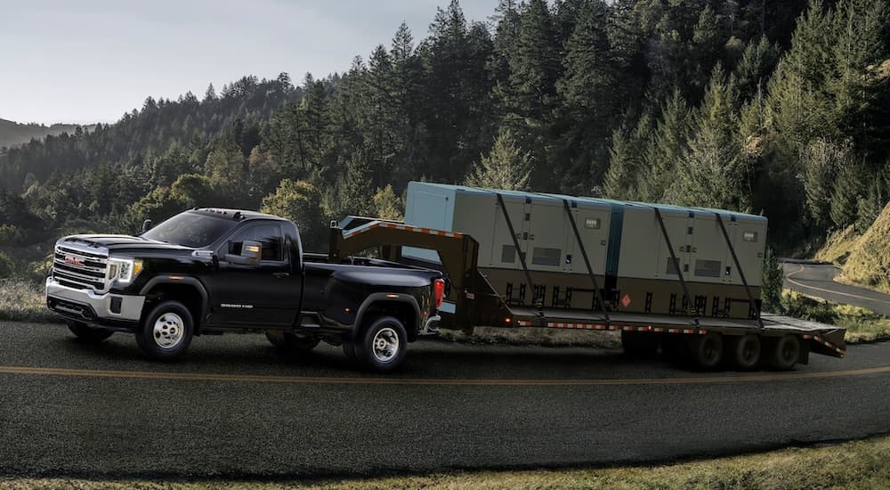 A black 2020 GMC Sierra 3500 HD is towing a gooseneck trailer up a mountain road.
