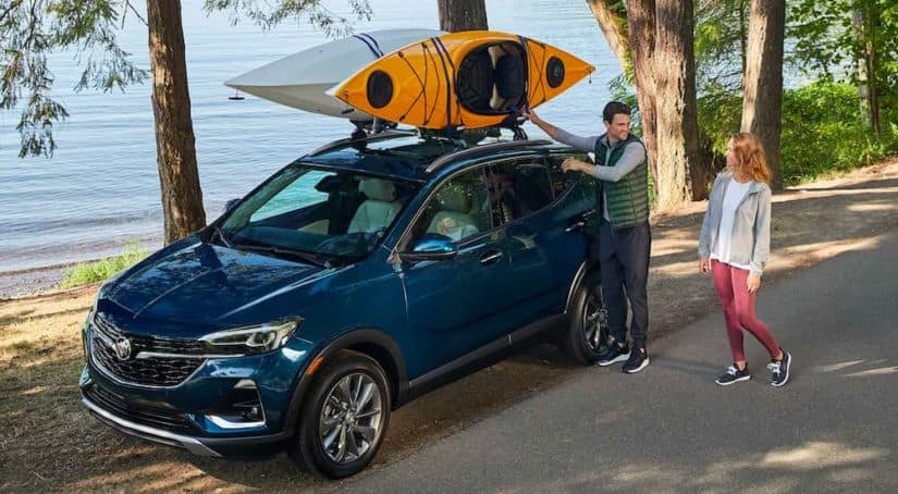 A dark blue 2021 Buick Encore GX is parked next to a lake with two kayaks mounted on the roof racks.