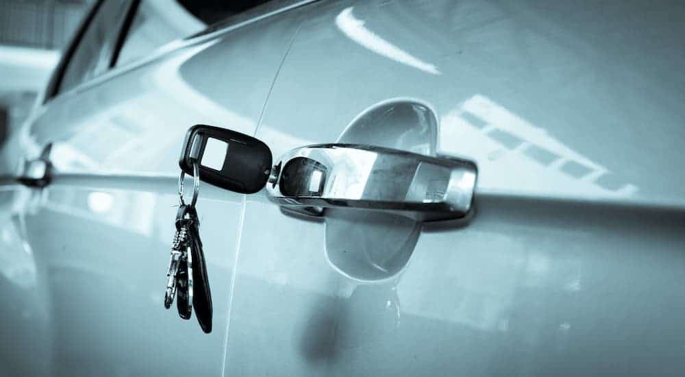 Car keys are shown inserted into the door handle lock of a silver car.