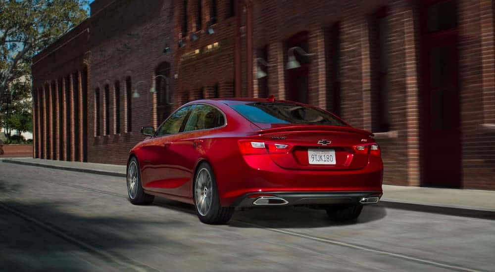 A red 2021 Chevy Malibu is shown from the rear driving by a brick building.