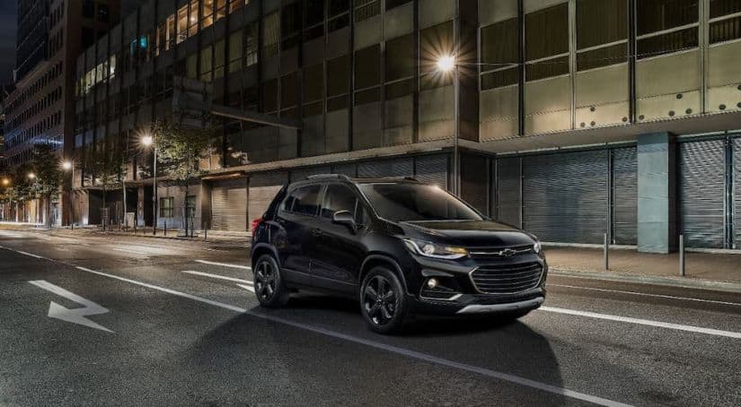 A black 2021 Chevy Trax is driving on a city street at night.