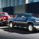 A dark blue 2021 Chevy Silverado 2500 HD LTZ is towing on old red pick up truck on a trailer.