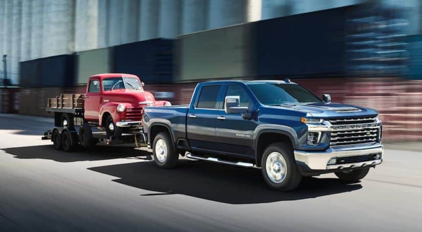 A dark blue 2021 Chevy Silverado 2500 HD LTZ is towing on old red pick up truck on a trailer.
