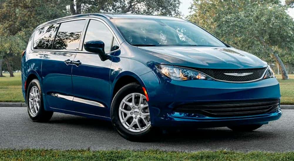 A blue 2021 Chrysler Voyager is parked on pavement in front of trees.