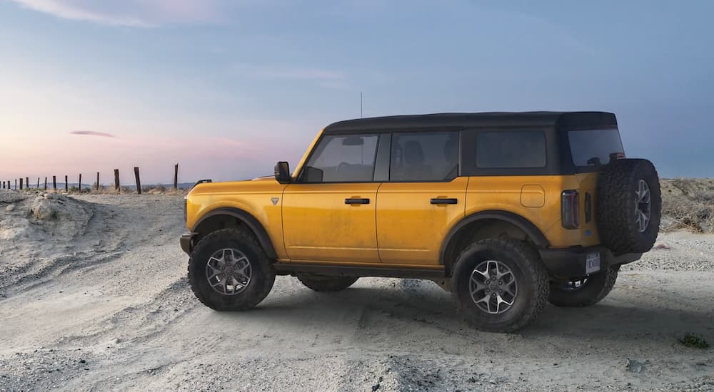 A yellow 2021 Ford Bronco Bandlands is parked on the beach with a jetti in the background.