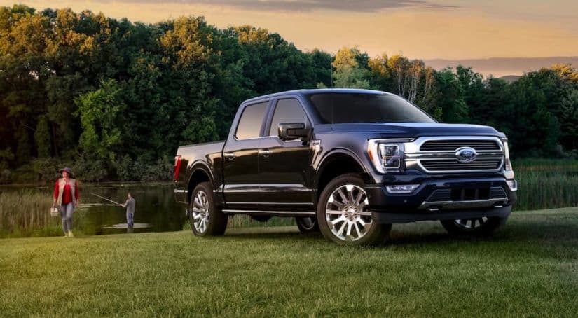 A dark blue 2021 Ford F-150 is parked near a pond with people fishing.