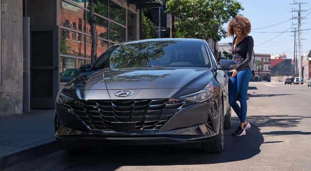 A dark grey 2021 Hyundai Elantra is parked in the city with a woman opening its door.