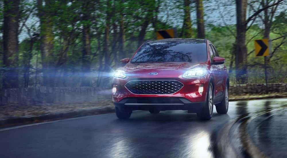 A red 2021 Ford Escape is driving down a wet road with its headlights on.