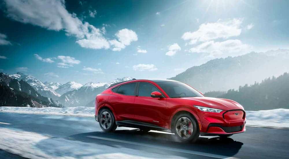 A red 2021 Ford Mustang Mach-E is driving though a snowy landscape.