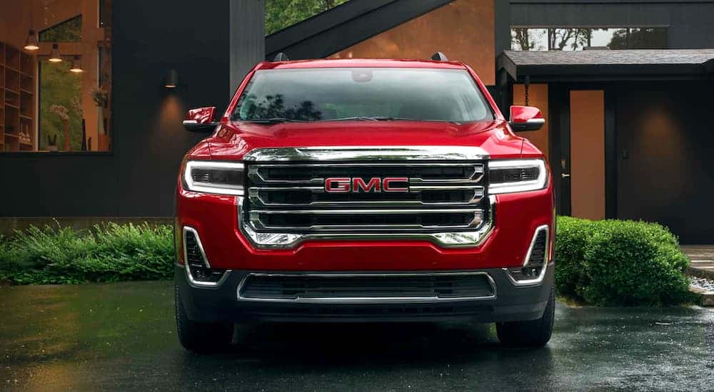 A popular GMC SUV, a red 2021 GMC Acadia, is shown in front of a modern house.