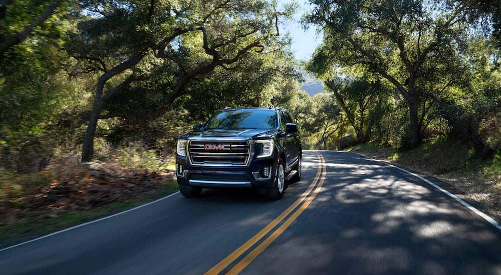 A black 2021 GMC Yukon is driving down a shady wood-lined road.
