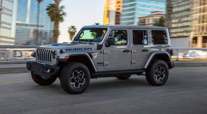 A grey 2021 Jeep Wrangler Rubicon 4Xe is driving down the road after leaving the Jeep dealership.