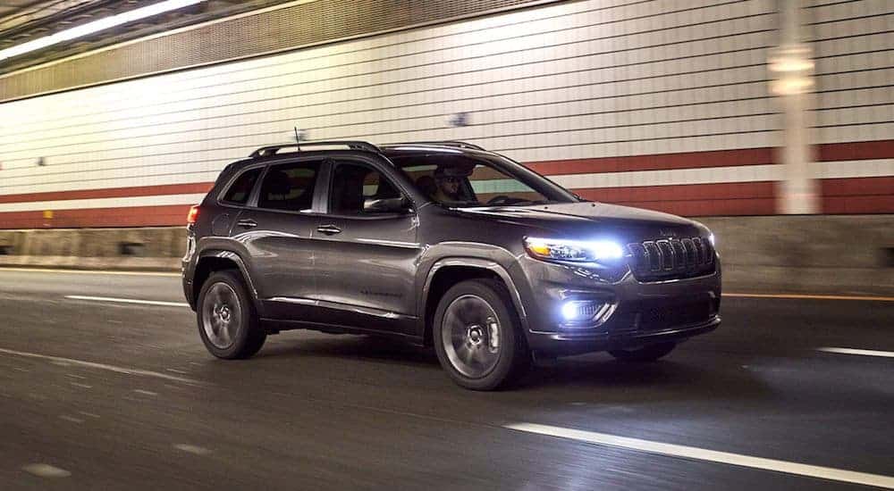 A popular Jeep SUV, a grey 2021 Jeep Cherokee, is driving though a tunnel with its lights illuminated.