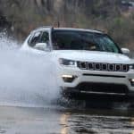 A white 2021 Jeep Compass is driving through a puddle splashing up water.