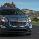 A blue 2016 used Chevy Equinox LT is driving down the road with hills in the background.