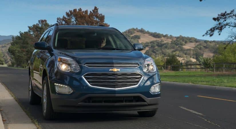 A blue 2016 used Chevy Equinox LT is driving down the road with hills in the background.