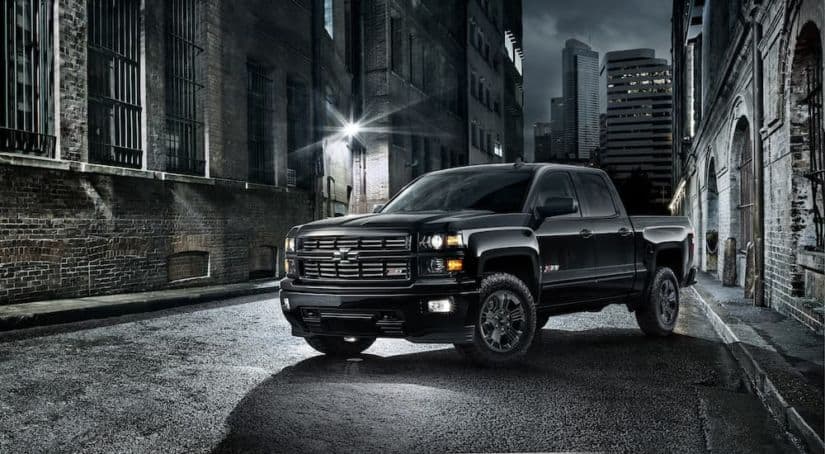 A black 2015 used Chevy Silverado Midnight Edition is parked on a city street at night.