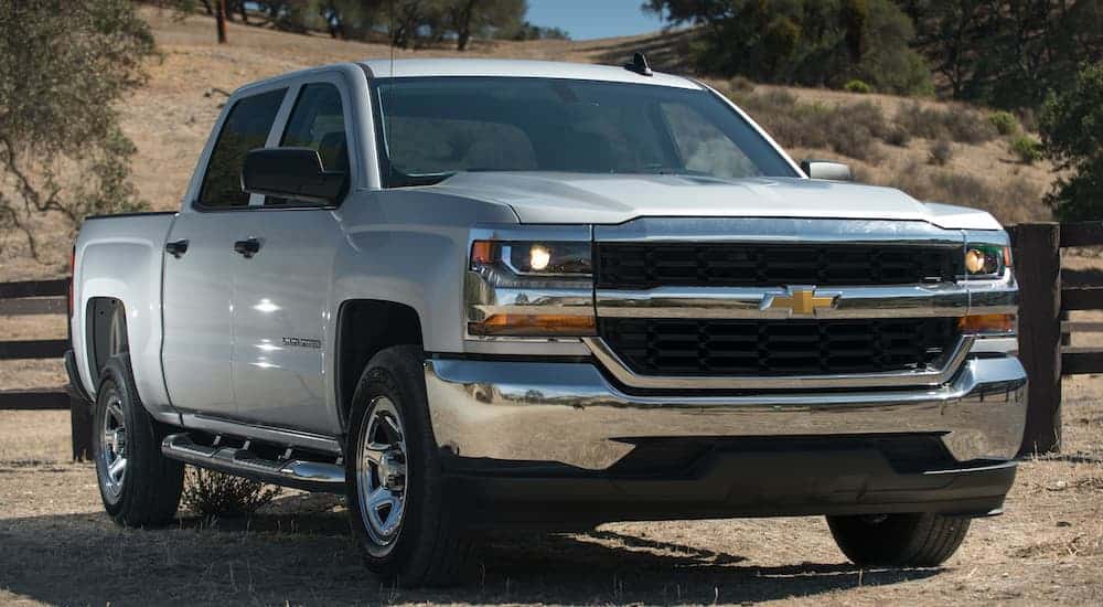 A silver 2017 used Chevy Silverado is parked in front of a brown fence angled right.