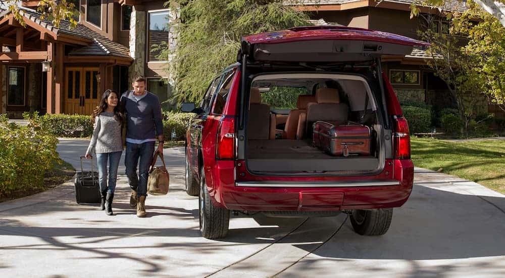 A couple is loading luggage into the back of a red 2020 used Chevy Tahoe.