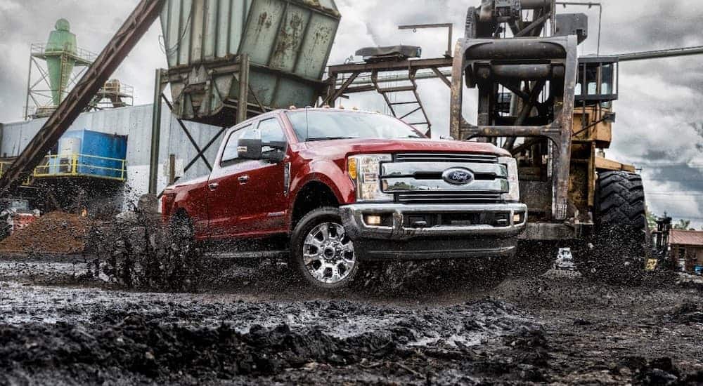 A red 2018 Ford F-250 Super Duty diesel is driving in mud in front of construction equipment.