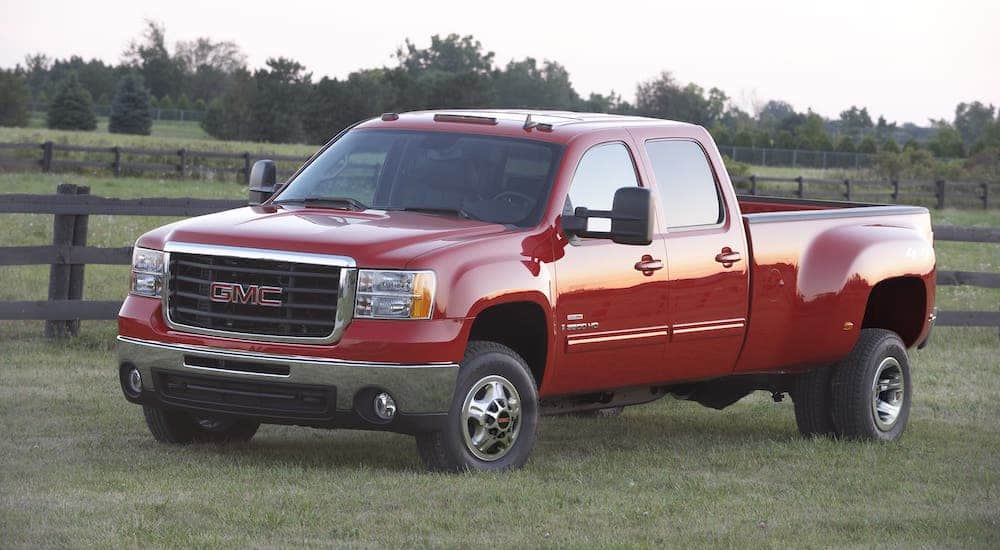 A red 2011 GMC Sierra 3500 diesel with dual rear wheels is parked in front of a fence.