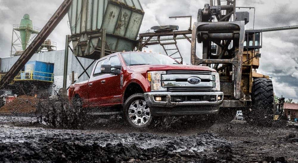 A popular used Ford diesel truck, a red 2018 F-250 Super Duty, is shown driving through mud in front of construction equipment.