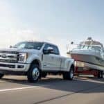 A white 2018 Ford F-350 diesel is towing a boat on a highway.