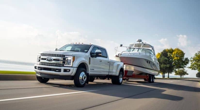 A white 2018 Ford F-350 diesel is towing a boat on a highway.