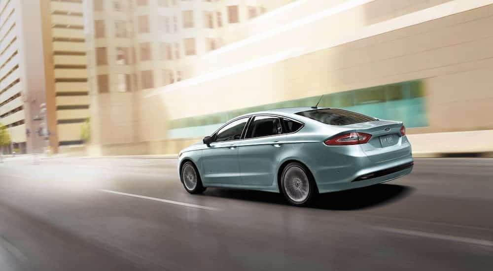 A light blue 2014 Ford Fusion Hybrid is shown from behind driving through the city.