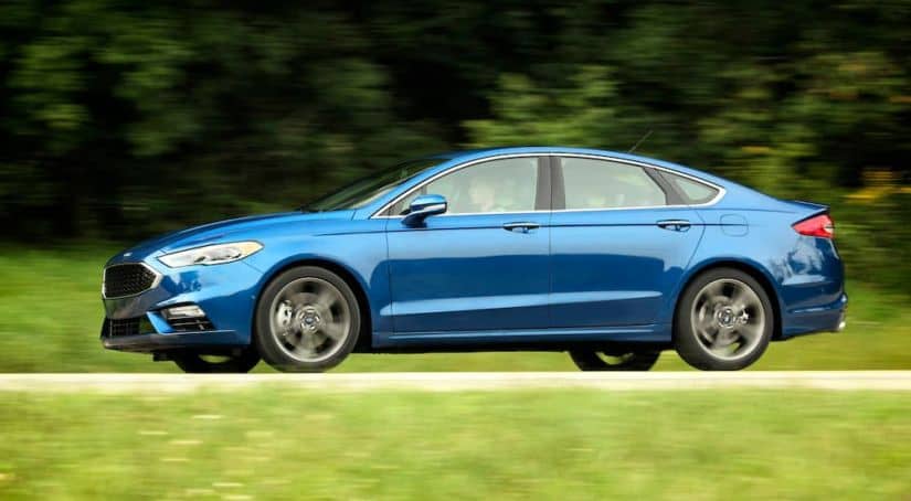 A blue 2017 used Ford Fusion Sport is shown in profile driving down the road.