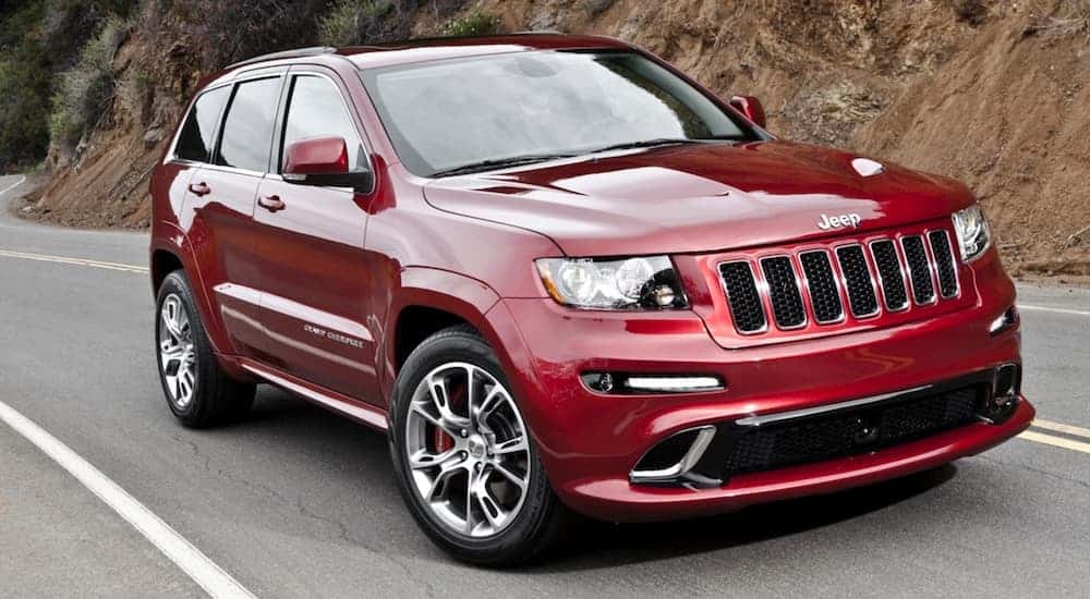 A red 2013 Used Jeep Grand Cherokee is on a winding road with a rocky slope behind it.