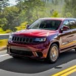 A red 2018 Used Jeep Grand Cherokee is driving past a guardrail and trees.