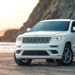 A white 2020 Used Jeep Grand Cherokee Summit is parked on the sand at a beach.