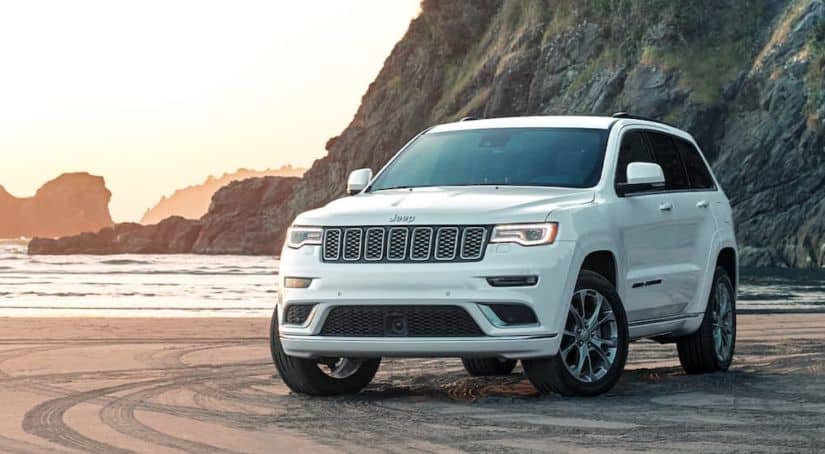 A white 2020 Used Jeep Grand Cherokee Summit is parked on the sand at a beach.