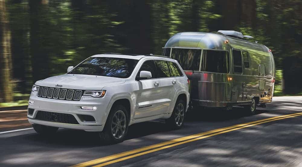 A white 2020 Used Jeep Grand Cherokee is towing an Airstream on a wooded road.