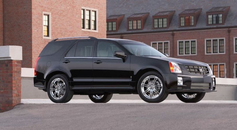 A black 2009 Cadillac SRX is parked in front of brick buildings after leaving the used luxury SUV dealer.