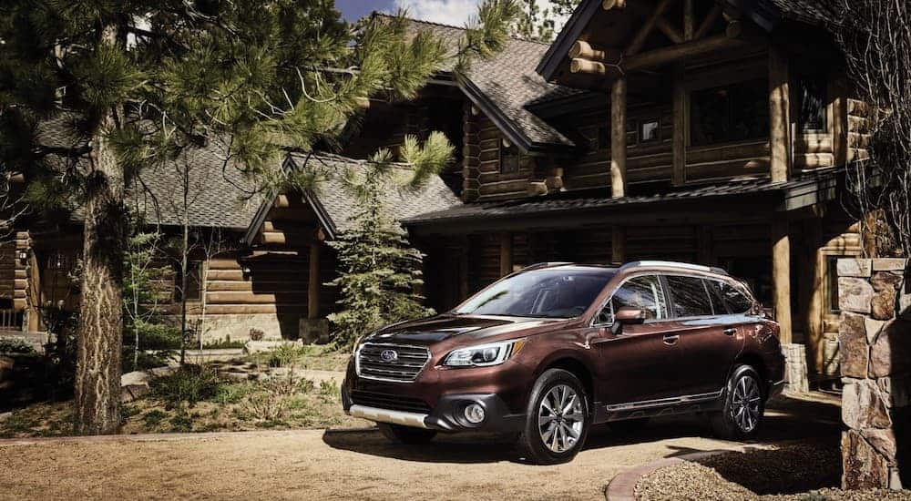A brown 2016 Subaru Outback is parked in front of a log cabin.