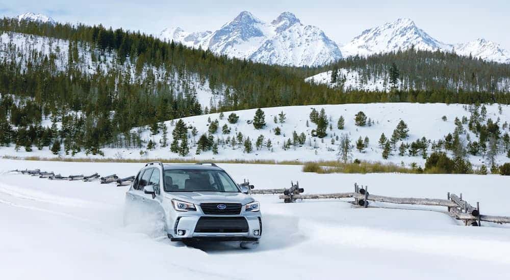 A silver 2017 used Subaru Forester is driving through the snow in the mountains.