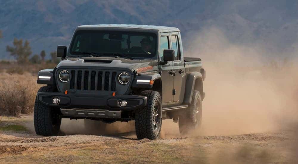 A black 2020 Jeep Gladiator Mojave is kicking up dust on a dirt road.