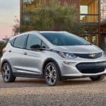 A silver 2021 Chevy Bolt is parked outside a modern house.