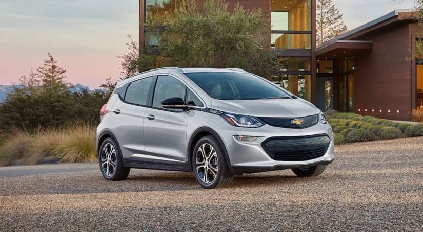 A silver 2021 Chevy Bolt is parked outside a modern house.