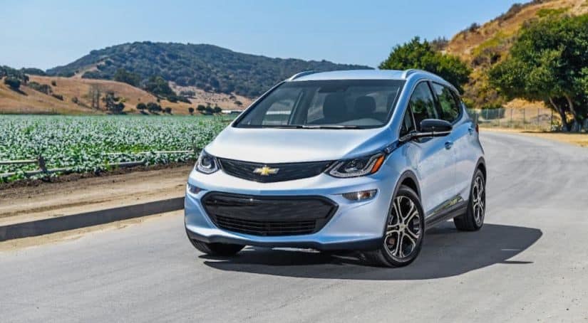 A silver 2021 Chevy Bolt EV is driving on a highway in front of mountains and fields.
