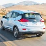 A silver 2021 Chevy Bolt EV is driving away on an empty highway towards mountains.