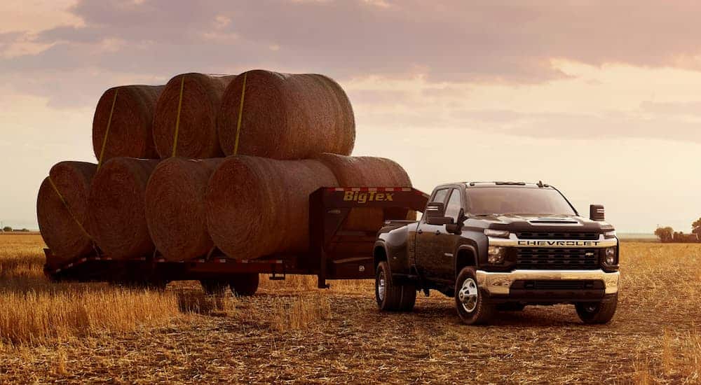 A black 2021 Chevy Silverado 3500 HD is parked in a field at sunset with hay bales on a trailer.
