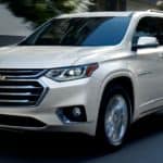 A white 2021 Chevy Traverse is driving on a city street.