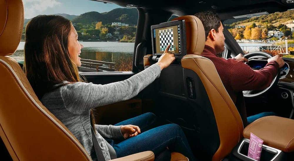 A young girl is playing chess on the rear screen in a 2021 Chrysler Pacifica with brown leather seats.