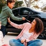A family is painting in a driveway in front of a black 2021 Chrysler Pacifica.