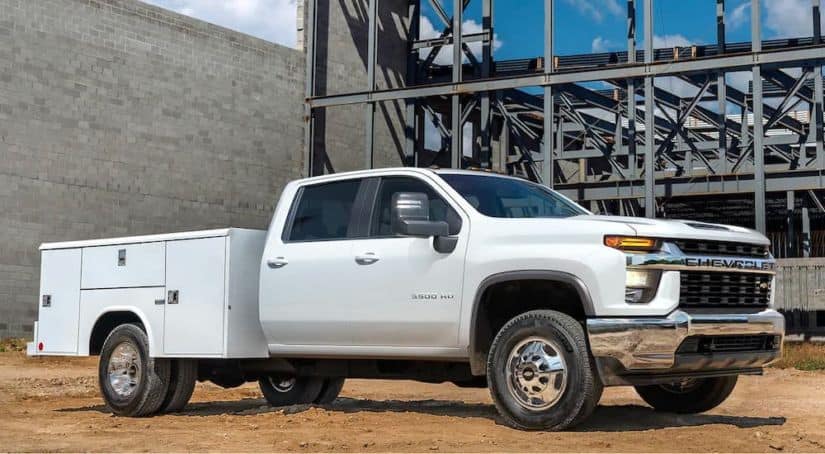 A popular 2021 commercial vehicle, a white Silverado Chassis Cab, is parked in front of a concrete building at a jobsite.