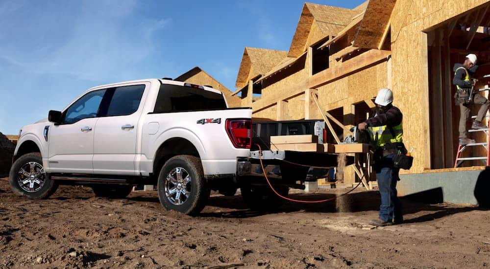 Construction workers at a house building site are pulling lumber out of a 2021 Ford Commercial vehicle, a white F-150.